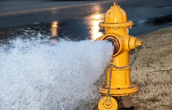 Yellow fire hydrant spraying water onto a street with wet pavement and grass visible in background